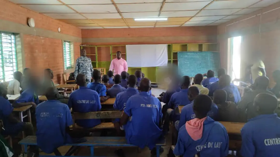 Séance de sensibilisation dans une salle de classe avec des personnes détenues en uniforme bleu, visages floutés.